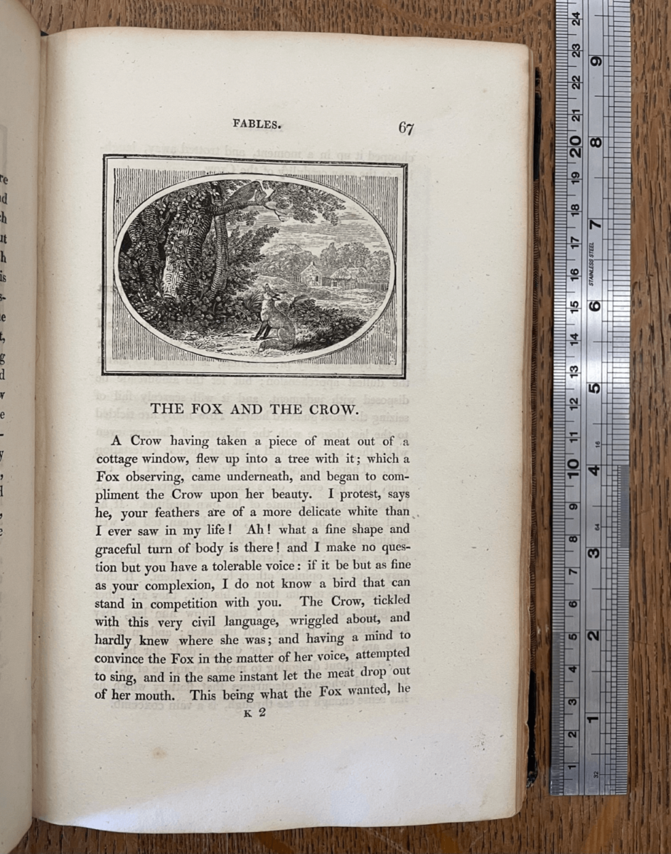 Photo shows a page from 'Aesop's Fables'. The image at the top of the page shows a fox looking up at a crow in a tree.
